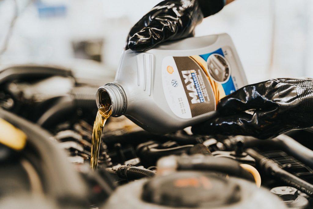 pexels-photo-13065697 Close-up of a mechanic pouring engine oil into a car engine, highlighting maintenance work.